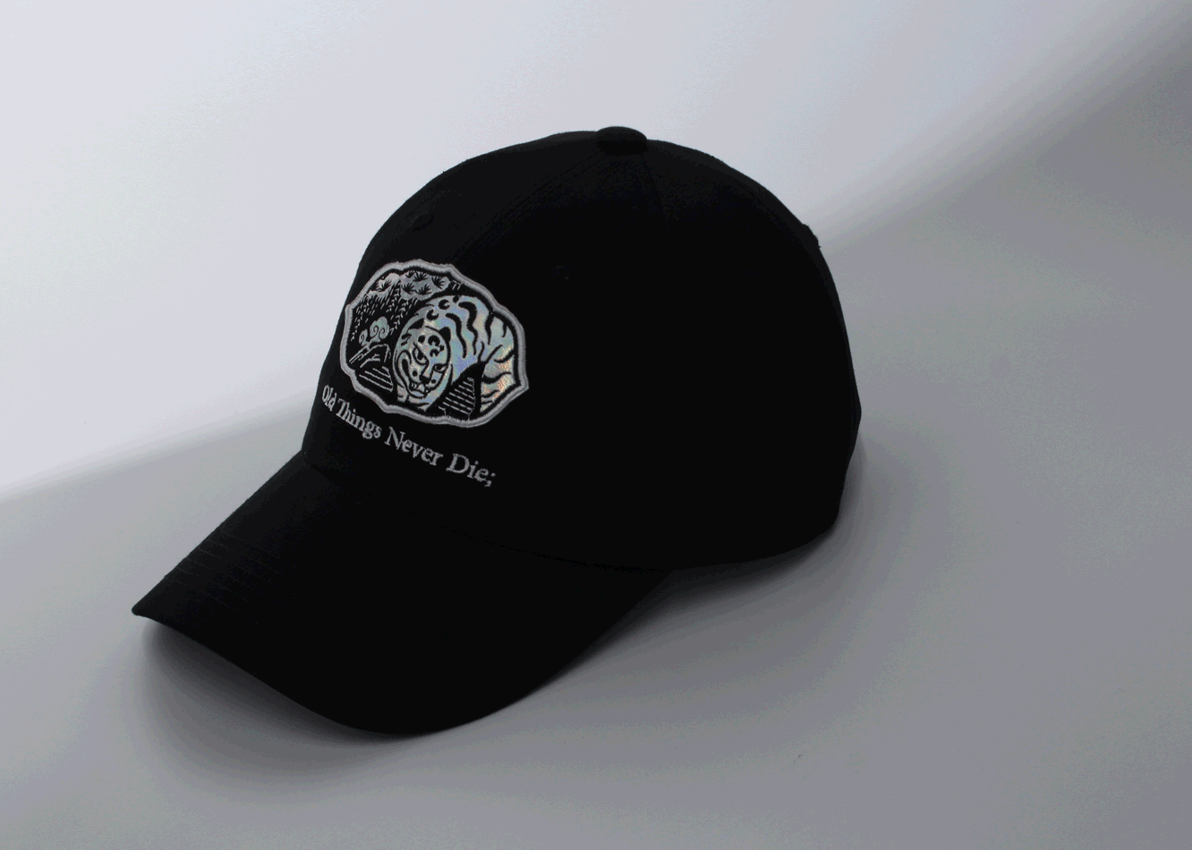 반짝이는 호랑이가 자수로 놓여있는 검은색 모자가 흰 배경에 놓여있고, 빛이 지나가는 모습